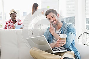 Businessman phoning and holding laptop on sofa