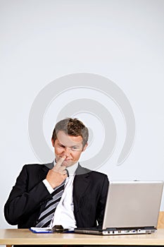 Businessman picking nose, looking at laptop in office