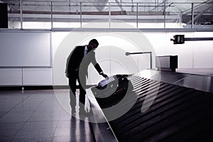 Businessman picking up suitcase on luggage conveyor belt, airpor photo