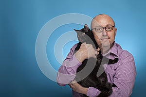 A businessman in a piked shirt holds a black cat in the hand