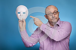 A businessman in a piked shirt holds a white mask, second face in his hand