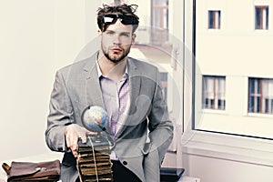 Businessman with pile of books and globe model on window background. Importance of knowledge concept. Cool guy wearing