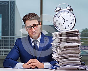 Businessman with pile stack of paper paperwork and an alarm cloc