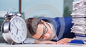 Businessman with pile stack of paper paperwork and an alarm cloc