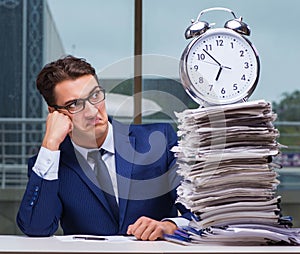 Businessman with pile stack of paper paperwork and an alarm cloc