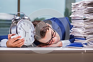 Businessman with pile stack of paper paperwork and an alarm cloc