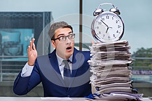 Businessman with pile stack of paper paperwork and an alarm cloc