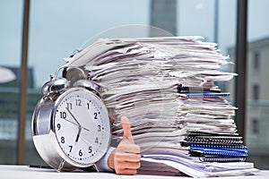 Businessman with pile stack of paper paperwork and an alarm cloc