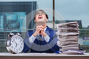 Businessman with pile stack of paper paperwork and an alarm cloc