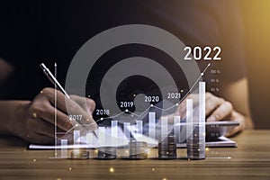 Businessman planning 2022 business growth on desk with virtual hologram chart graph