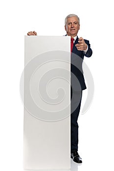 Businessman pointing at the camera and holding a blank billboard