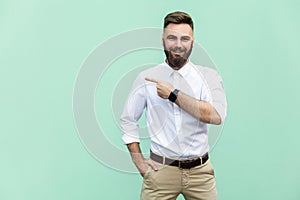 Businessman pointing copy space. Handsome young adult man with beard in white shirt looking at camera and pointing away while stan