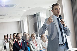 Businessman pointing while speaking through microphone during seminar in convention center