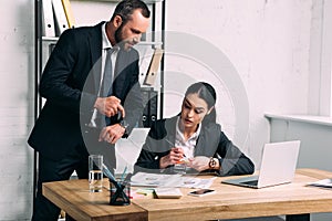 businessman pointing at watch near concentrated businesswoman at workplace with laptop