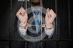 Businessman or politician with handcuffs behind bars in prison cell