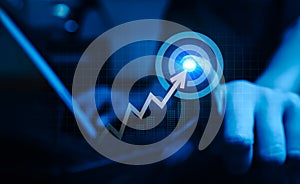 Businessman pressing on big target dart icon with rising arrow graph for upward revenue.