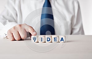 Businessman pressing his finger on the wooden cubes with the word idea and a light bulb icon. Idea creation in business