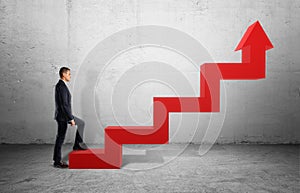 Businessman in profile walking up big red arrow in form of ladder