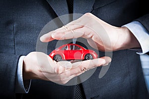 Businessman protect with his hands a red car, concept for insurance, buying, renting, fuel or service and repair costs