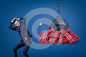 Businessman protecting himself with hands and chained ball with a `DEBT` sign over red dynamite sticks with lit fuse on