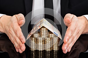 Businessman protecting house made of currency at desk