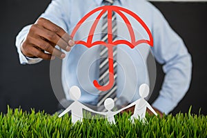 Businessman protecting paper cut out family with umbrella