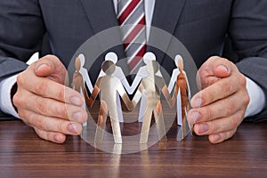 Businessman protecting team of paper people on desk