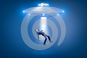 A businessman pulled toward an open hatch of a UFO by some invisible force.