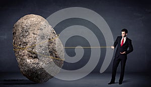 Businessman pulling huge rock with a rope