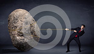 Businessman pulling huge rock with a rope