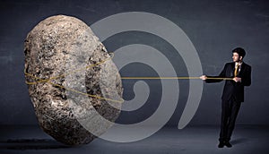 Businessman pulling huge rock with a rope