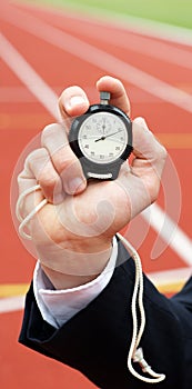 Businessman pushes start button of stopwatch - sports ground in the back