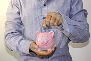 A businessman put a coin in a pink piggy bank and saved the money to plan ideas.