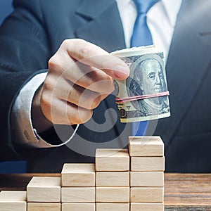 Businessman puts a dollars bundle on top of stairs. Business success, company profitability. Raising bids, increase interest rate