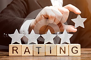 Businessman puts the fifth star above the word Rating on wooden blocks. The concept of the high rating of hotels and restaurants.
