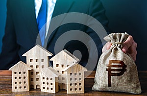 A businessman puts a philippine peso money bag near the houses.