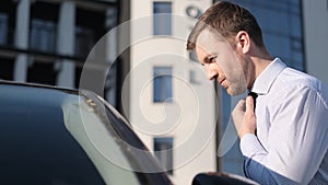 Businessman puts on a tie on the street, looking out the window of his car. Unpunctual man.