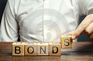 Businessman puts wooden blocks with the word Bonds. A bond is a security that indicates that the investor has provided a loan to