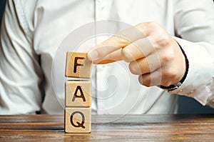 Businessman puts wooden blocks with the word FAQ frequently asked questions. Collection of frequently asked questions on any