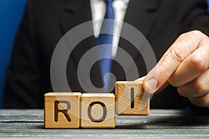 Businessman puts wooden blocks with the word ROI. Return on investment concept. Profitability and loss-making of investments. ROMI