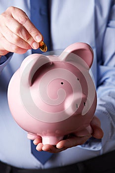 Businessman Putting Coin Into Large Piggy Bank