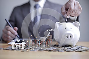 businessman putting coin on the piggybank with icon family on wooden table, donation