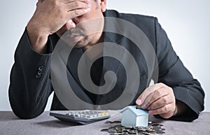 Businessman is putting coin into small house piggy bank, and feel stressed