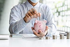 Businessman putting coin into small piggy bank at business desk