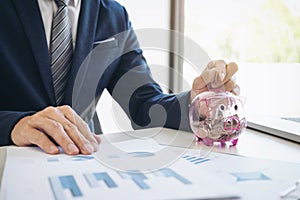 Businessman putting coins into piggy bank and using calculator t