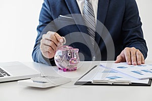 Businessman putting coins into piggy bank and using calculator t