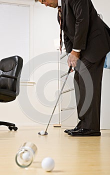 Businessman putting golf ball in office