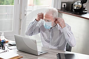 Businessman putting on medical face mask and working on laptop from home