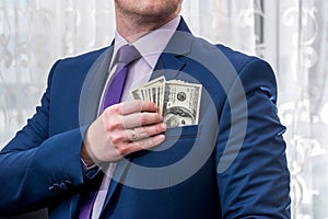 Businessman putting us money into his suit pocket.