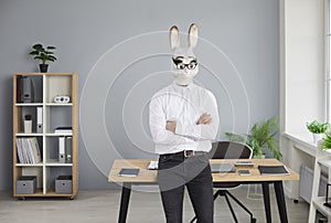 Businessman in rabbit head mask standing with folded hands in office